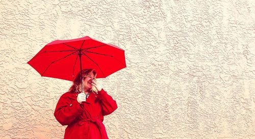 Full length of woman holding red umbrella standing on rainy day