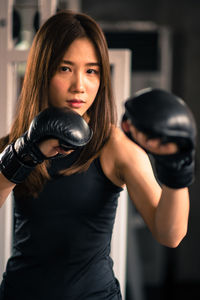 Portrait of confident young woman practicing boxing while standing in gym