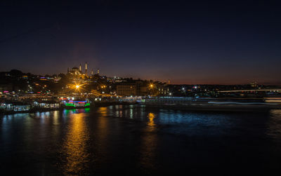 Illuminated city by river against sky at night