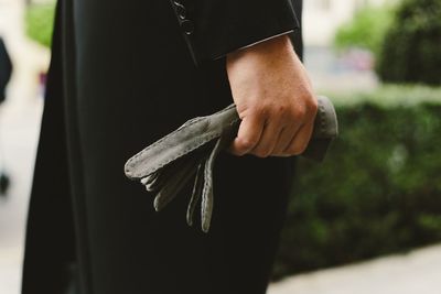 Midsection of man holding gloves while standing outdoors