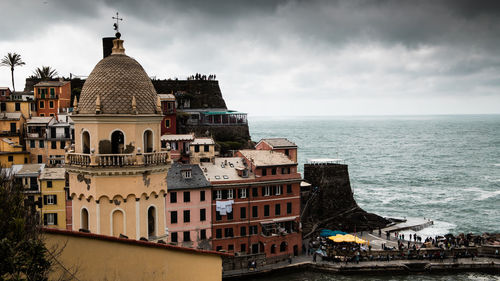 Buildings by sea against cloudy sky