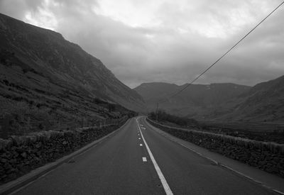 Empty road leading towards mountains against sky