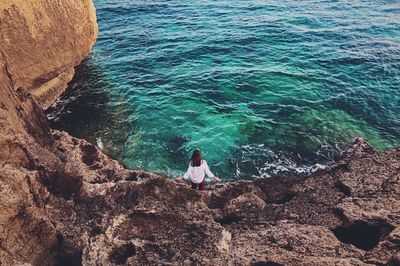 High angle view of woman sitting on rock by sea
