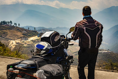 Man motorcyclist watching valley from hill top with his loaded motorcycle and pristine natural view