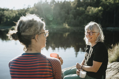 Two senior women sitting on rock at lakeshore