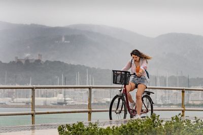 Man sitting on railing by mountains against sky
