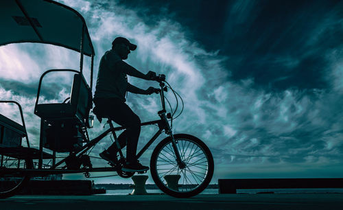 Silhouette man with bicycle against sky