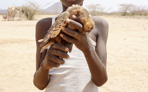 Midsection of boy holding dead bird at desert during sunny day