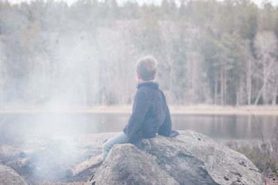 Young boy sitting on a rock by a campfire and lake in sweden