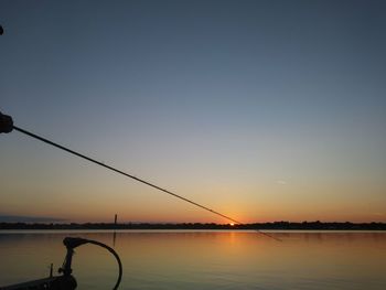 Silhouette fishing rod by sea against clear sky during sunset