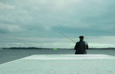 Man fishing in sea against sky