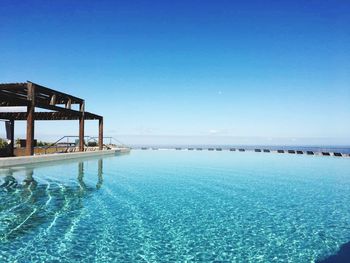 Swimming pool by sea against clear blue sky