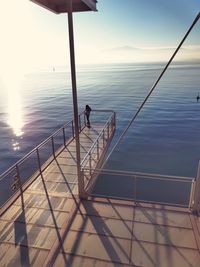 Man on railing by sea against sky