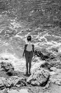 Rear view of woman standing on rock at beach