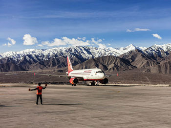 View of man and airplane on airport runway against sky