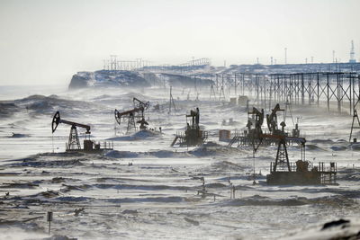 Oil pumps on snow covered field against clear sky