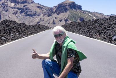 Portrait of smiling man gesturing while crouching on road