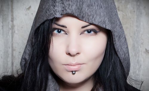 Close-up portrait of young woman wearing hooded shirt by wall