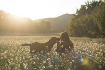 Young woman and her dog in field of flowers at twilight