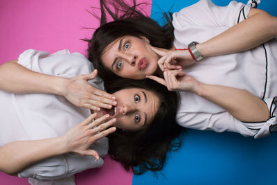 Directly above shot of female friends making face while lying on colored background