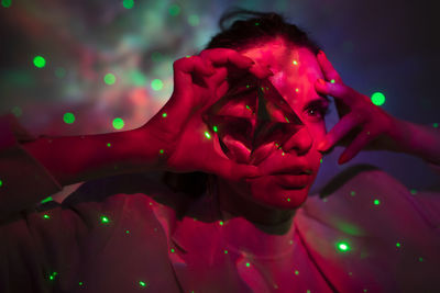 Close-up of woman holding crystal against illuminated background