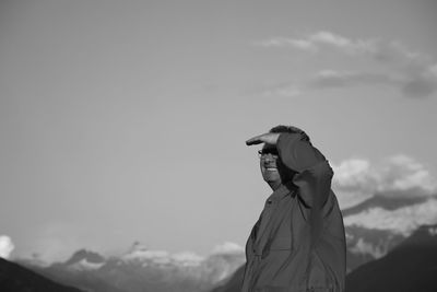 Man shielding eyes while looking away against sky