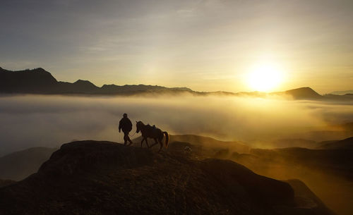 Silhouette man and horse on mountain cliff