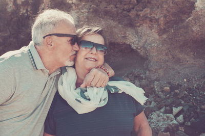 Senior man kissing woman sunglasses against rock