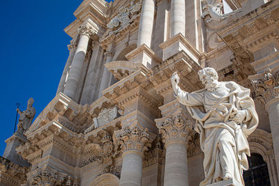 A statue of the ortigia cathedral with columns behind it, siracusa.