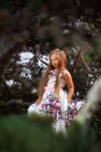 Portrait of young woman standing against trees