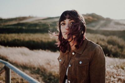 Portrait of young woman sitting against land