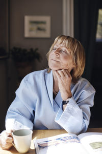 Senior woman with hand on chin holding coffee cup while relaxing at table