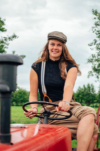 Smiling young woman sitting in park against sky