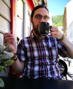 Portrait of man drinking while smoking cigarette at outdoor cafe