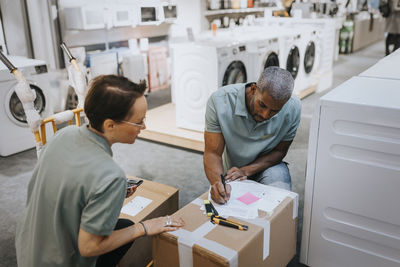 Saleswoman looking at salesman writing in document on box at appliances store