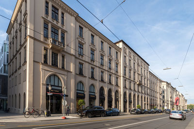 Cars on road by buildings in city against sky