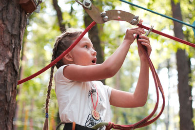 Low angle view of girl attaching safety harness on rope in forest