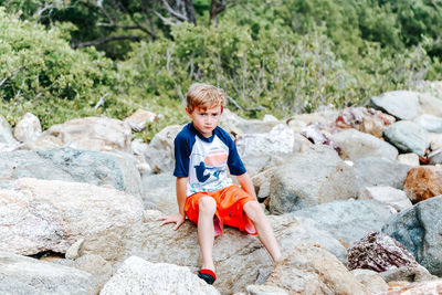 Boy sitting on rock outdoors