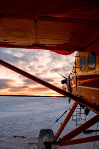 Airplane on snow covered field against sky during sunset
