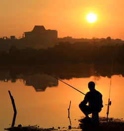 Silhouette people fishing in sea during sunset