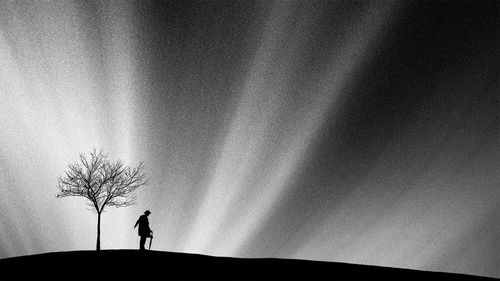 Low angle view of silhouette man standing by bare tree against cloudy sky
