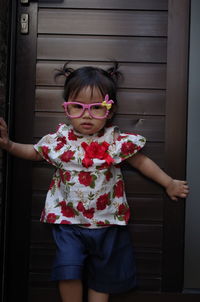 Portrait of cute girl wearing eyeglasses standing against door