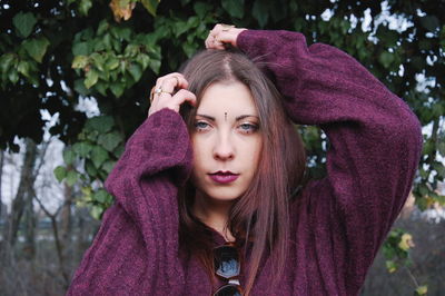 Portrait of beautiful young woman with long hair standing against trees