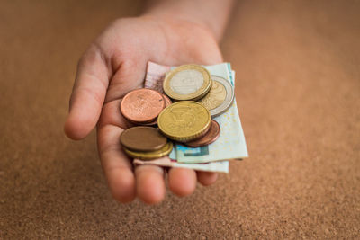 Close-up of hand holding coins and paper currency on table