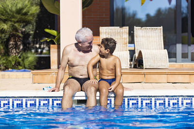 Full length of shirtless man sitting in swimming pool