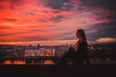 Woman standing by river against sky during sunset