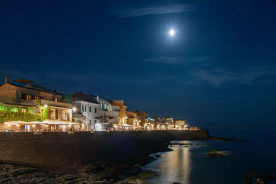 Buildings by river against sky at night