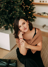 A beautiful pretty young woman in an elegant outfit celebrates christmas and decorates the house