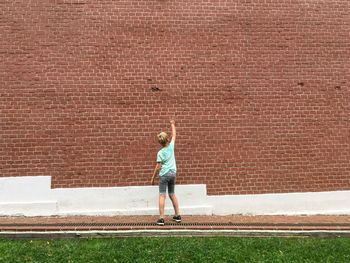 Rear view of boy standing against brick wall