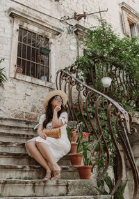 Portrait of beautiful young woman sitting on stairs of old stone house